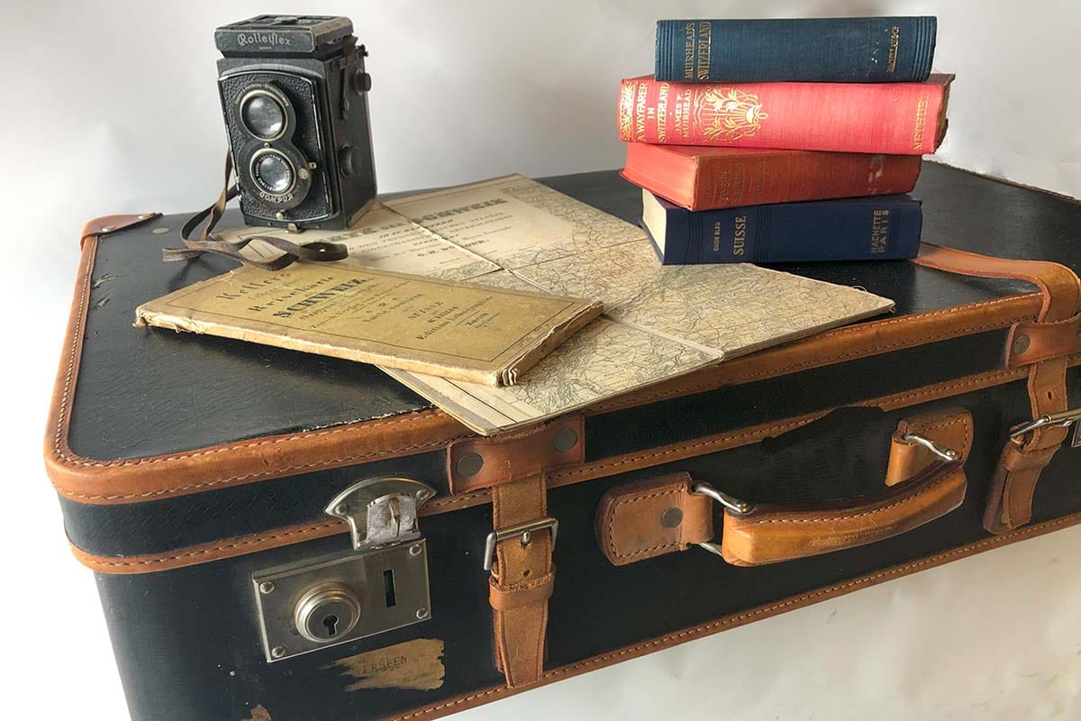 Bild mit einem historischen Koffer, einer alten Kamera und antiquaren Büchern und Reiseführern.